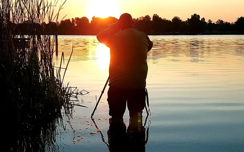 Sven fotografiert im flachen Wasser eines Sees bei Sonnenuntergang